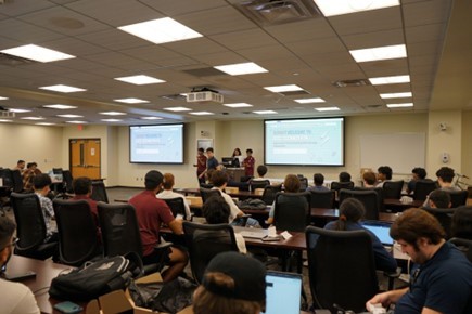A picture of the presenters and stage with attendees in view.